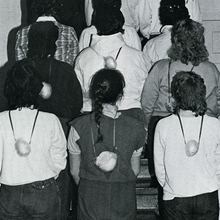 A photo of a group of female students with their backs to the camera, wearing onions around their necks.  Or are they?