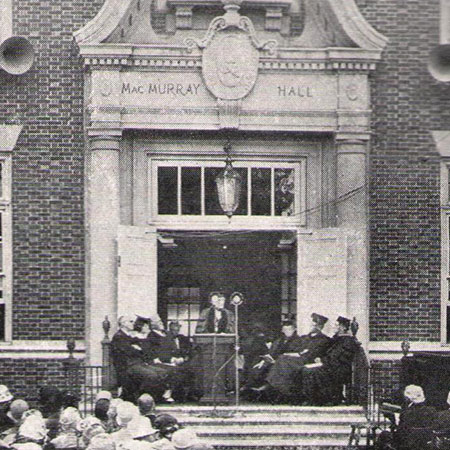 A photo of Jane Addams standing at a lecturn in the doorway of MacMurray Hall.